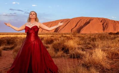 blonde female singer in red dress in front of Uluru. Cultural tourism