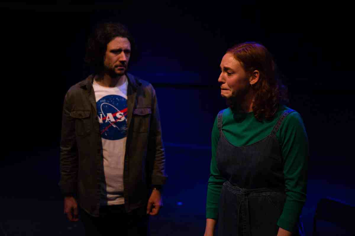 two actors on stage, one male and one female, looking concerned and upset