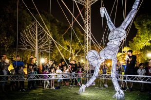 a giant puppet made of wire being manipulated by puppeteers in a park at night