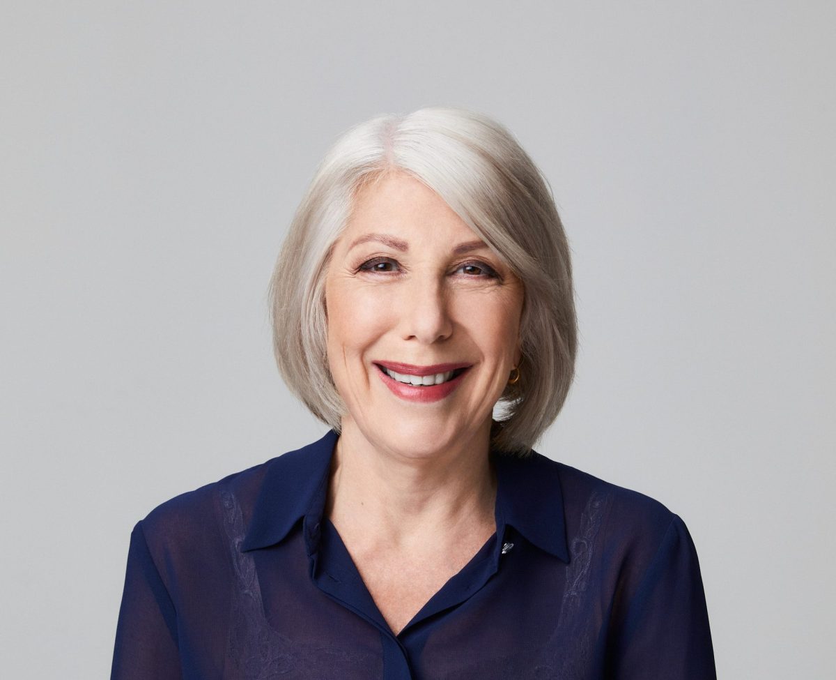 A grey-haired woman in a purple dress on a grey background