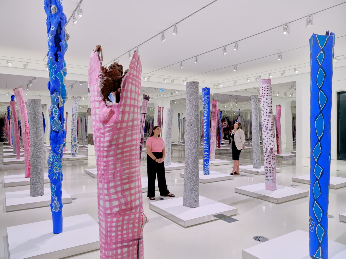 Two women stand in installation of bark painting at NGV Interntional, Melbourne