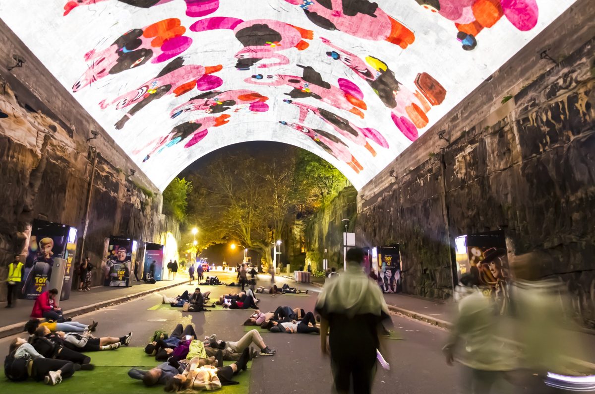 a group of people in a laneway under a light installation