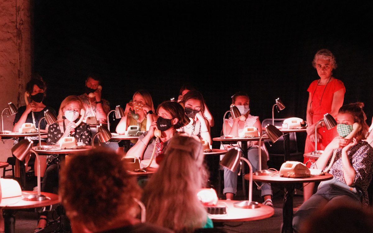 a scene from Roslyn Oades' The Nightline where the audience are listening to audio on old telephones in a room with a performer