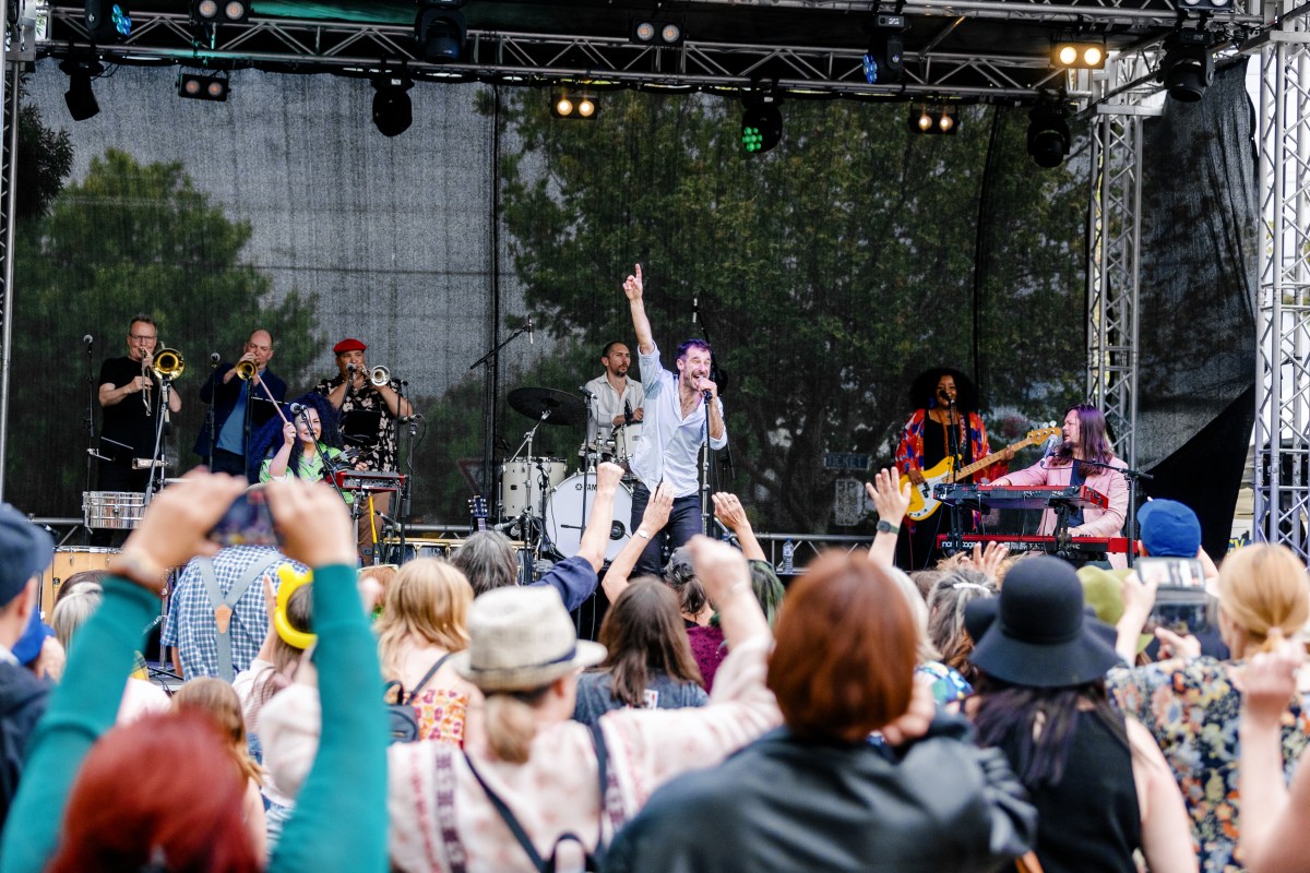 A singer with microphone has fist raised, seen by the young audience who are cheering Singer with fist raised who are cheering live music.