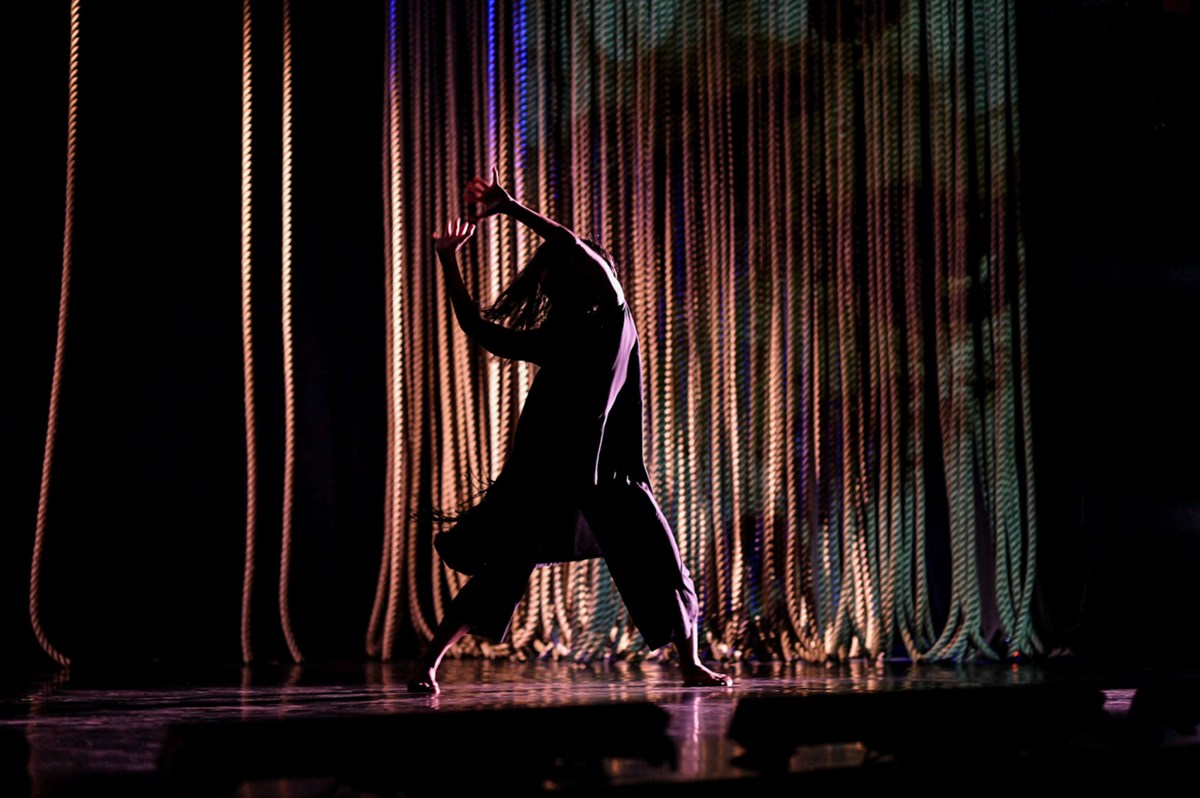 Mutiara, Marrugeku. Perth Festival. A dancer in silhouette in front of a curtain of ropes.