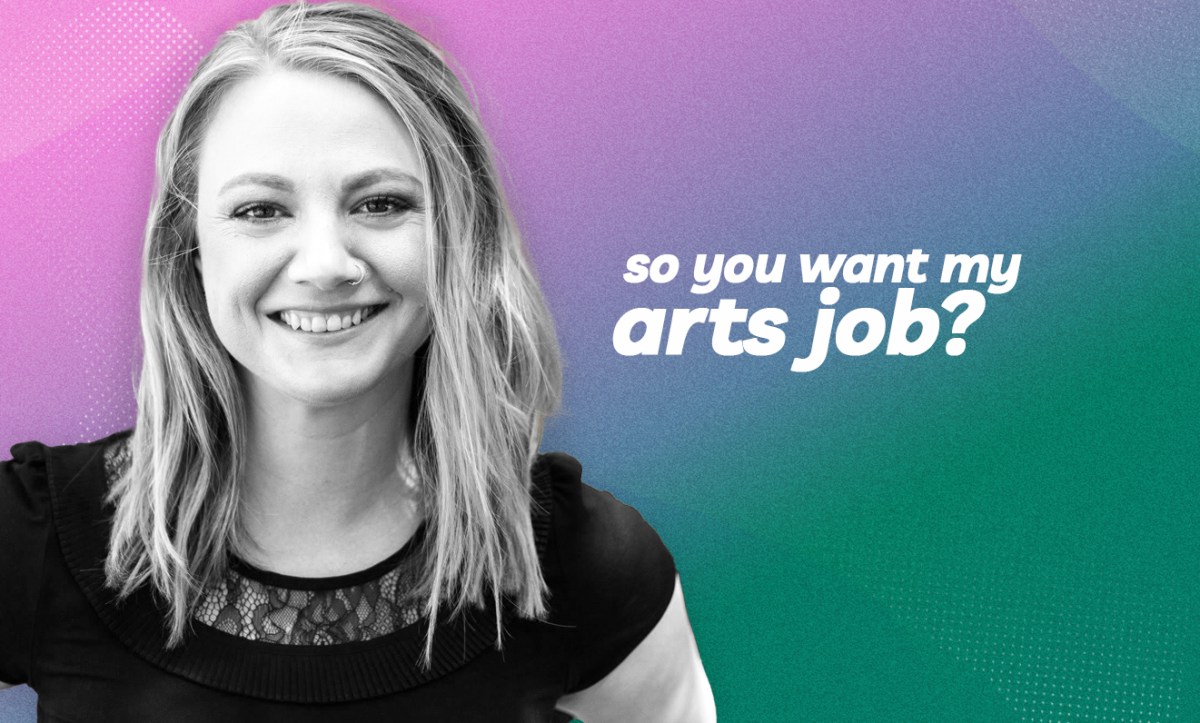 Emily Sheehan. Photo: Supplied. A young white woman with shoulder-length blonde hair and smiling at the camera. She is wearing a black tshirt and standing in front of a vibrant wall mural.