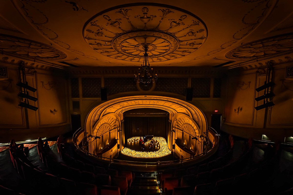 Candlelight: A Tribute to Mitski. Image is a old theatre stage with a string quartet surrounded by dozens of battery operated candles.