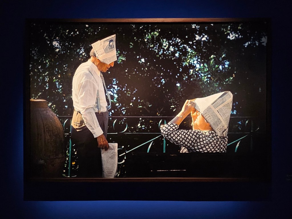 Work from ‘Through the playful eyes of Elliot Erwitt’, installation view at Fotografiska Shanghai. Photo: ArtsHub. The photo depicts an elderly couple wearing paper boat hats in a park environment. 
