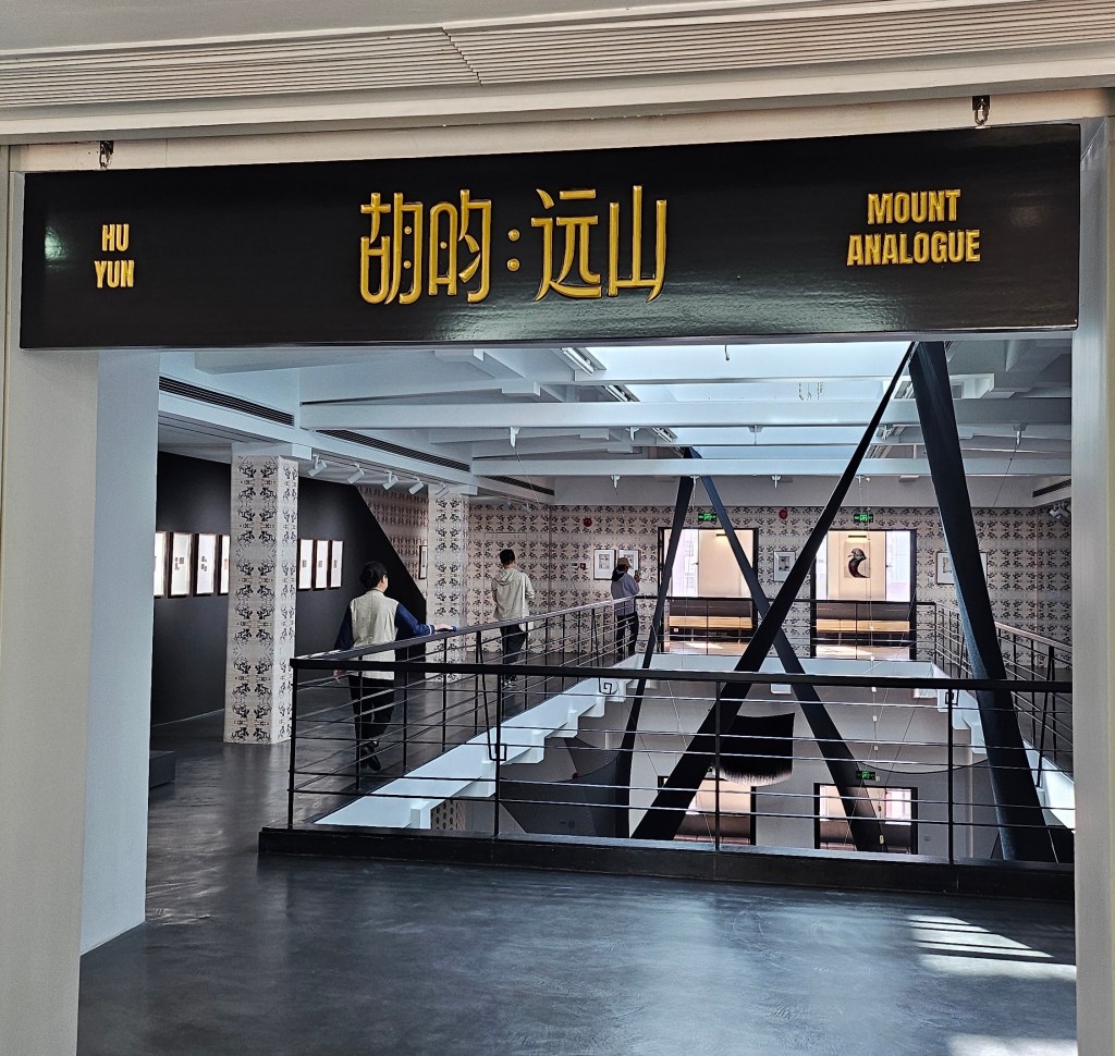 ‘Hu Yun: Mount Analogue’, installation view at Rockbund Art Museum. Photo: ArtsHub. A view into a gallery space with the centre hollowed out to reveal the floor below. On top of the door frame is a sign that says ‘HU YUN / MOUNT ANALOGUE’ alongside Chinese characters of the same phrase. 