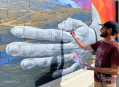 Nevada murals. A close-up of a giant hand being painted in a mural by a Caucasian man in a baseball cap.