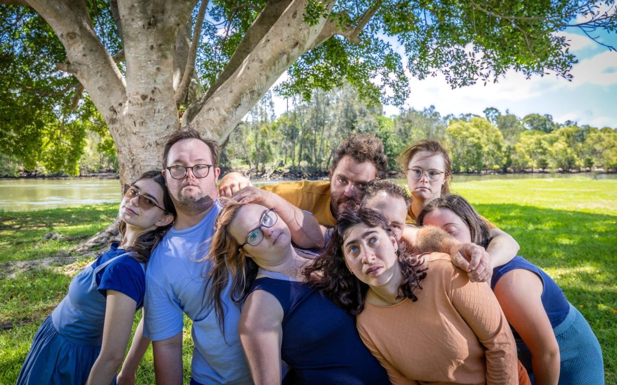 Sprung!! Integrated Dance Theatre Inc, recipient of Create NSW’s Arts and Cultural Funding Program. Photo: Thomas Oliver. Outdoor in a park setting, a group of eight ensemble members from Sprung lean on each other. They appear relaxed.