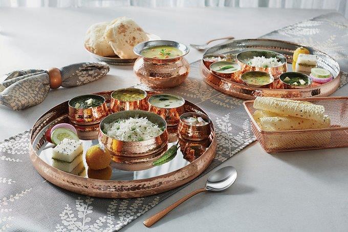 A restaurant photo of sauces, condiments and rotis in small copper dishes on a grey patterned table runner and with a matching napkin in a ring. The Art of the Table.