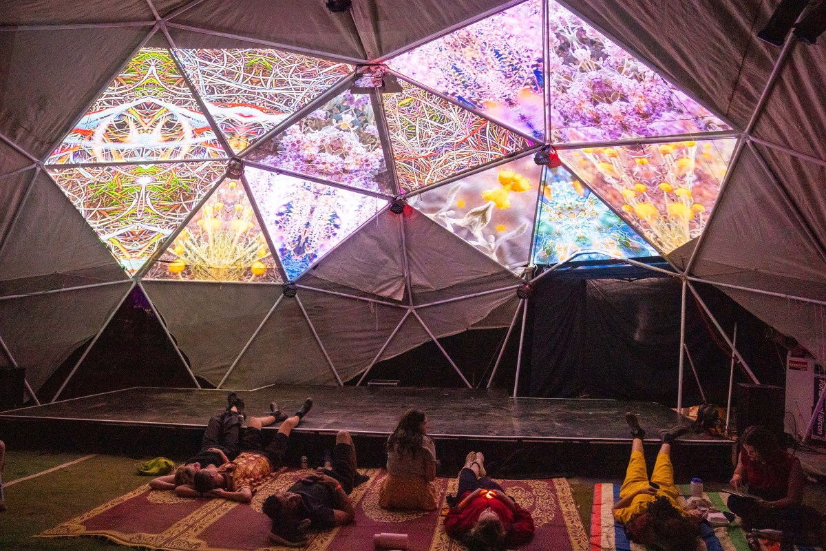 A group of people lie on mats underneath a fabric geometric cover, with hexagonal brightly lit parts, that are multicoloured