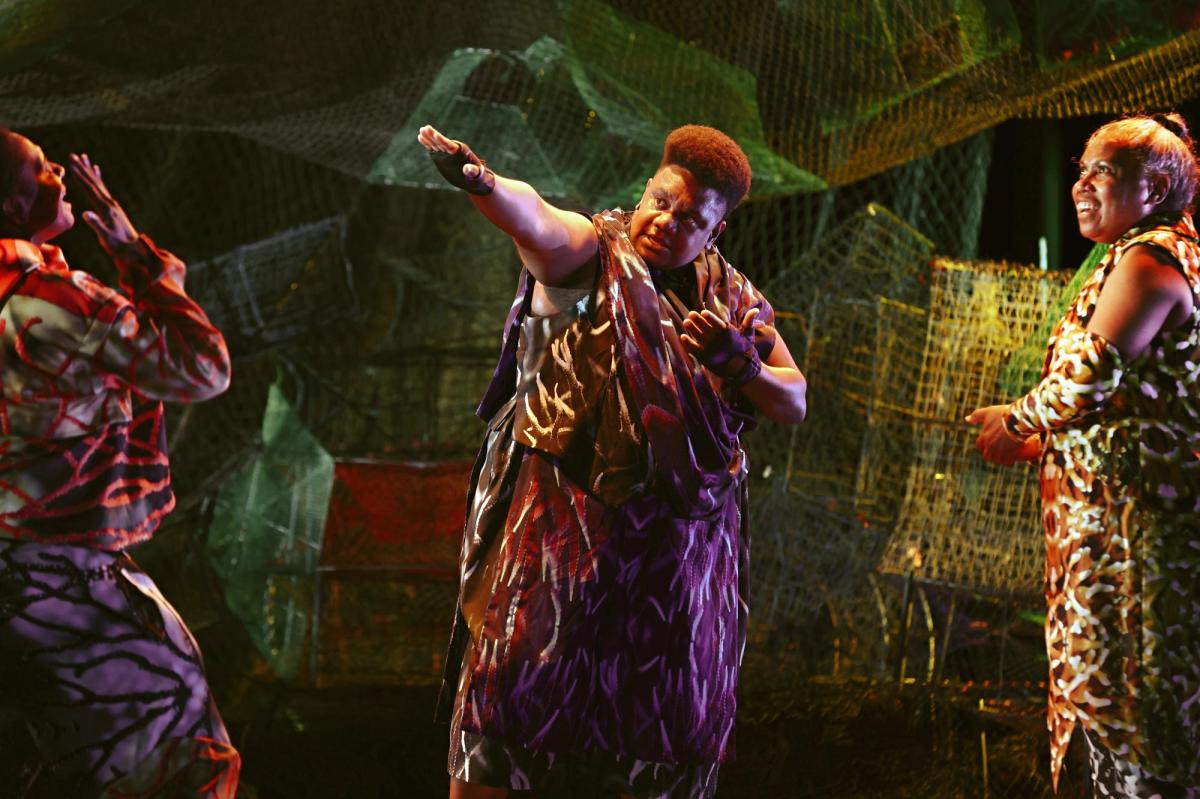 Three women in colourful printed clothes stand in front of assorted wire baskets that are also lit up.