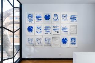 A grid of 18 prints in shades of blue are attached on a wall.