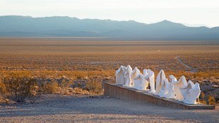 Nevada Art Trail. An installation in the desert with mountains in the background of a line of white concrete figures representing Christ and the disciples at the last supper. Only their cloaks are visible, the statues are empty.
