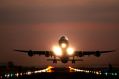 A jumbo jet takes off from a brightly lit runway at night, semi-silhouetted against the evening sky.