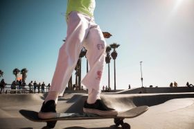 on the move. image is bottom half of person wearing pink trousers and green shirt on a skateboard in a skatepark.