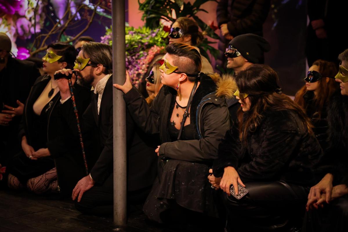 A crouching crowd all in black wearing gold masks.