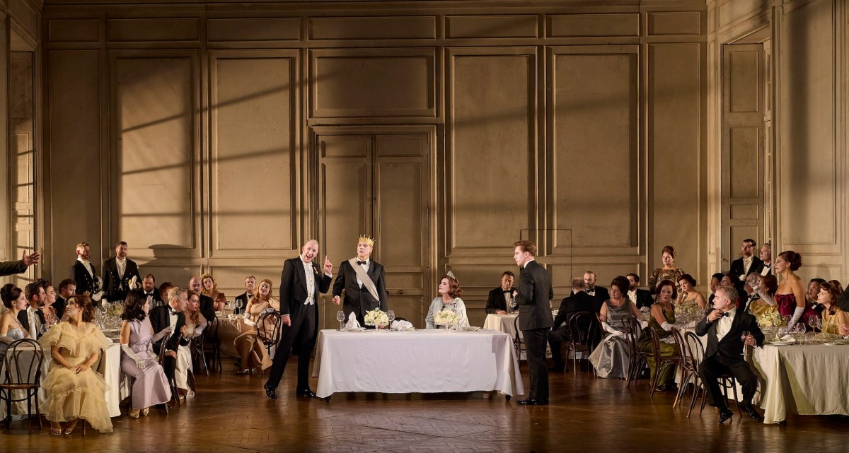 A banquet scene with a group of formally dressed diners singing opera in a high ceilinged banquet hall.