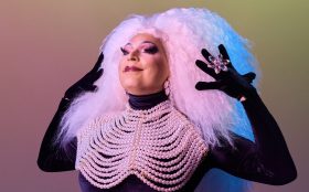 Ben Graetz as Miss Ellaneous. Photo: Mia Mala McDonald for Queering the Collection. A big drag personality with pink curly hair, bold makeup, long black gloves and a collar made out of pearls.