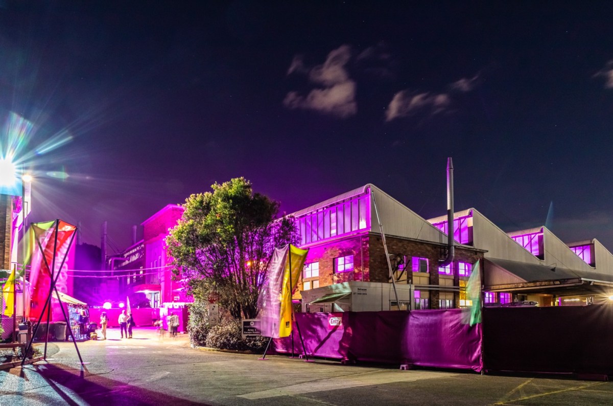 An industrial warehouse at night is lit up in pink and spotlights.