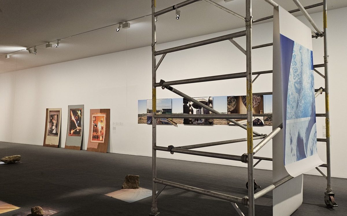 ‘Built Photography’ installation view at MAPh, featuring a print hanging from a scaffold on the right hand side, printed photographic images leaning against a wall and fabric printed pieces on the ground.