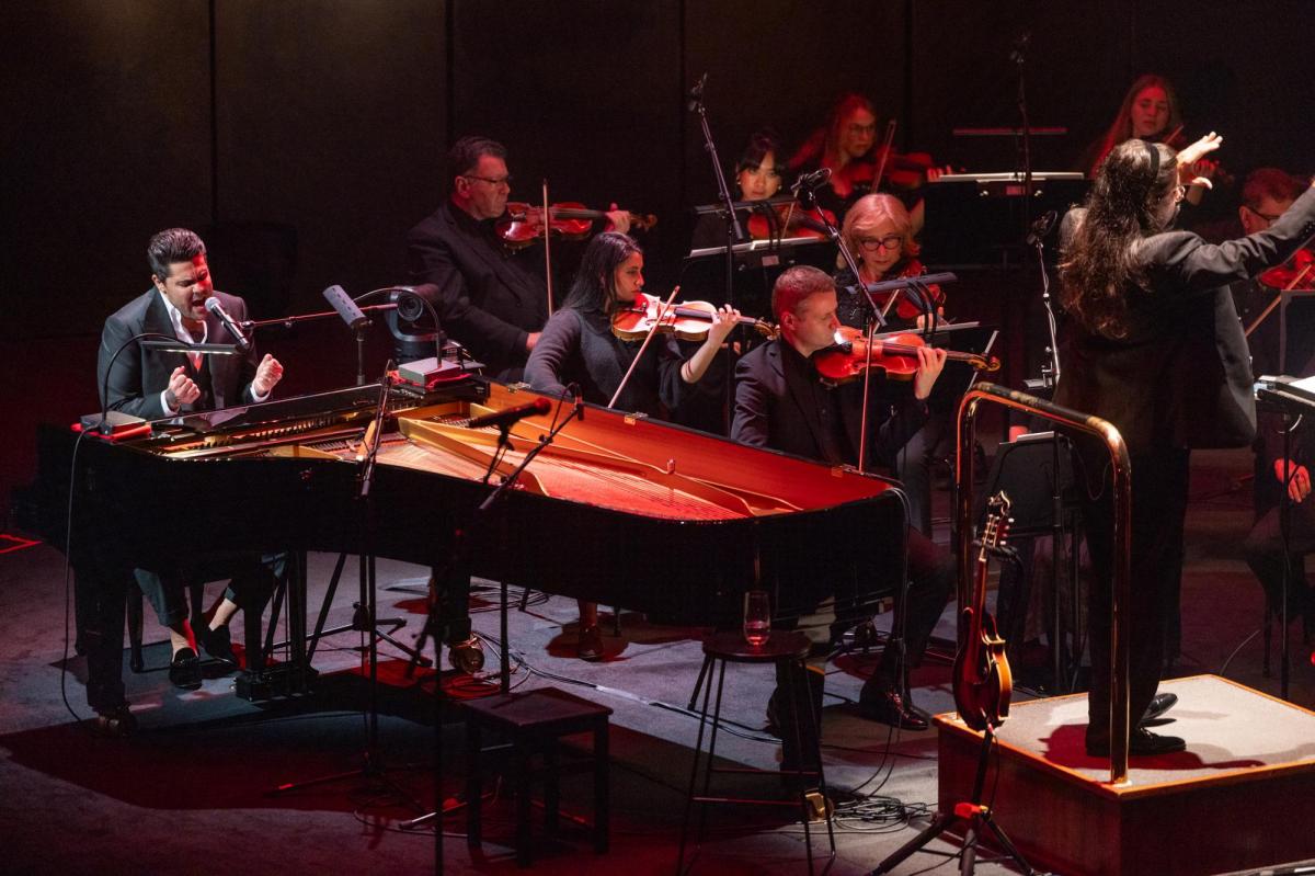 MSO. Dan Sultan. A man is seated at a piano on the left. He's singing. In the background are an orchestra of strings. A conductor is on the right.