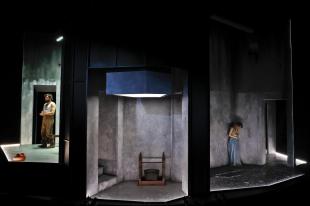 Three panels. A man is on the left, a woman on the right. The middle section is bare except for a wooden household object. The panels are lit inside but there is darkness surrounding them.