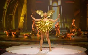 Finalists for 2024 World of WearableArt Competition announced, including Sol Invictus, who was also a finalist of 2023 WOW. A model wearing a golden wings on her head and an armour resembling the sun, standing in a power pose with more performers in the background.
