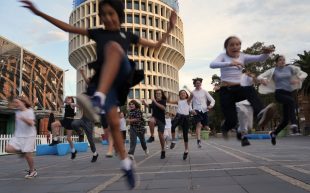 Tantrum Youth Arts brings 'WonderCity' to New Annual, featuring an ensemble of young performers. Photo from a low angel as kids run and jump across a concrete pathway outdoors towards the camera.