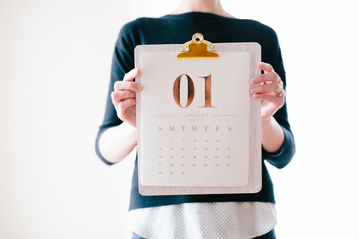 Woman wearing navy blue jumper holding up a page of a calendar. Exhibition planning.