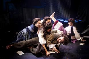 Four young women and a young man are laughing and playing, mid tumble on the floor.