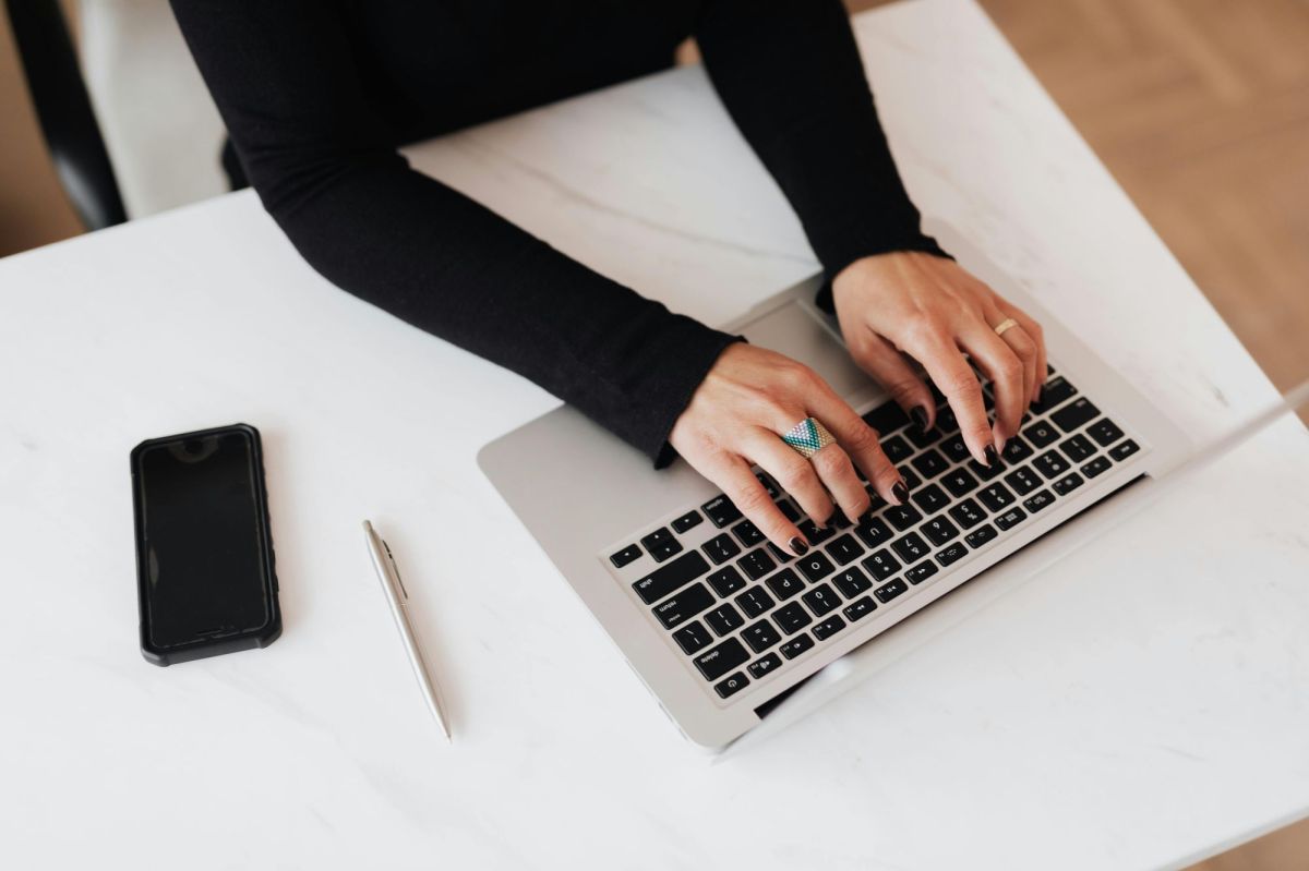 a birds eye view of a pair of women's hands reaching to laptop keyboard.