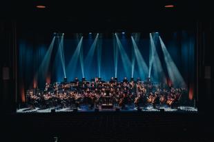 A photo of a full orchestra with a row of spotlights shining down on them. Music of Hans Zimmer.