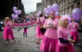 Artists dressed in pink and purple promote their show on a grey street at Edinburgh Fringe.