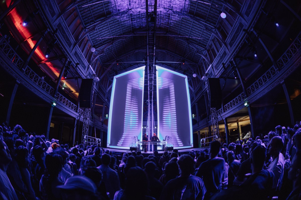 Sleep D performing at the Royal Exhibition Building as part of Now or Never 2024. In a cavernous hall dancers look towards huge screens with abstract purple and blue imagery.