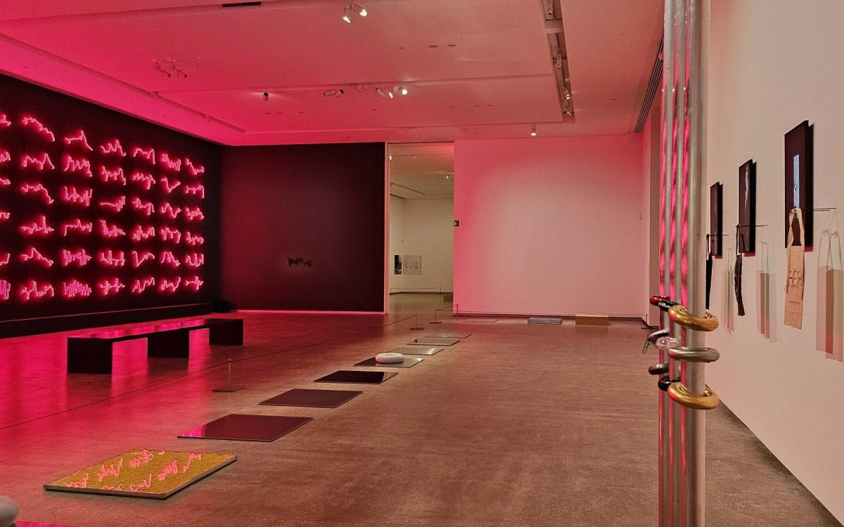 ‘(SC)OOT(ER)ING around Su san Cohn and Eugenia Raskopoulos’, installation view at TarraWarra Museum of Art. On the left is a red neon installation of cardiograms and to the left is a metal installation of three poles with doughnut bracelets. In the centre are a series of square surfaces lying on the floor.