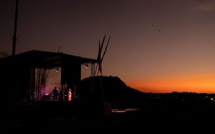 2024 Regional & Remote Music Summit. A photo of a stage seen from afar against the sunset of a natural environment.