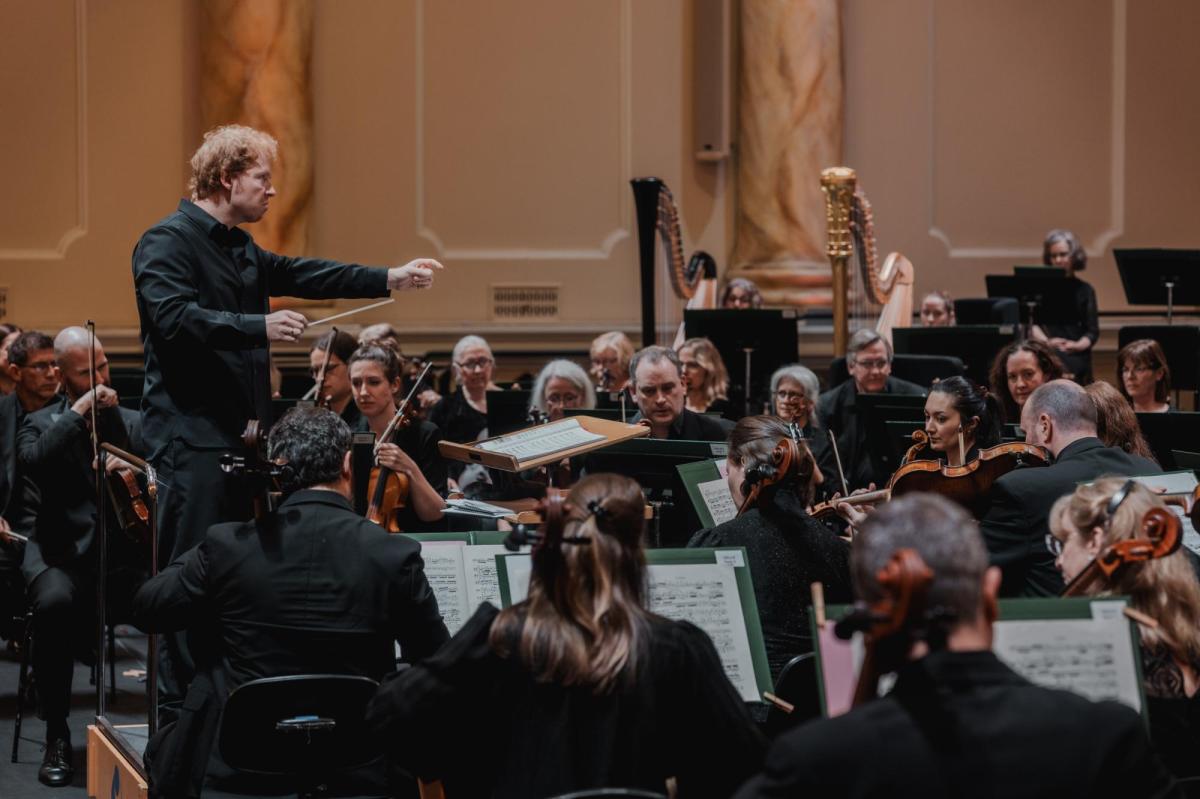 An orchestra scene, with a conductor at the left and musicians on the right.