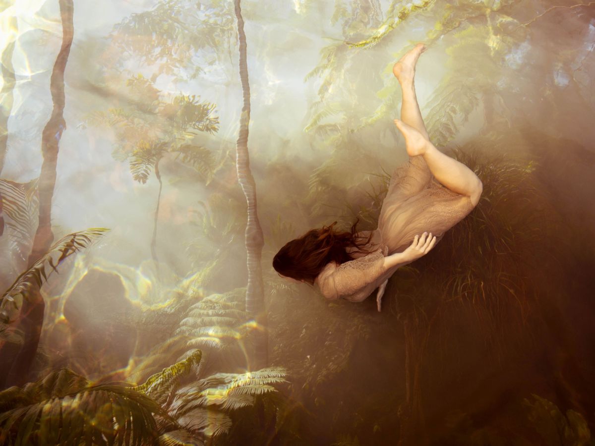 A woman in a flimsy dress swims underwater in a dreamy artistic netherworld.