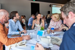 Culture Business. Image is a group of business people sitting around a table comparing notes and networking.