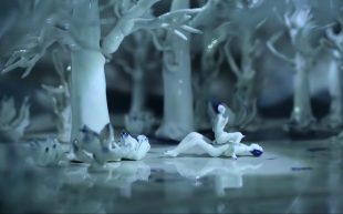 Still from short film ‘Mr Sea’ by Geng Xue, part of group exhibition ‘ Overseas Locals 2024: Blossoms of Chinese Contemporary Art in Melbourne’. Two miniature blue and white porcelain characters sitting atop of one another in a darken forest filled with white porcelain trees.