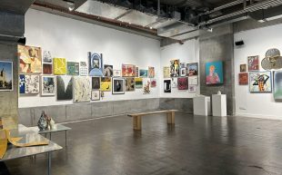 ‘No Vacancy Annual’ at No Vacancy Gallery in Melbourne’s central business district. The concrete and industrial gallery space is filled with paintings and drawings on its white walls, with smaller sculptures and objects on display on white plinths and raised metal platforms.