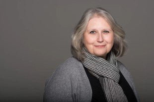 Jo Davies is a grey-haired, fair-skinned, middle-aged woman wearing a grey and black scarf, a grey cardigan and a black shirt. Jo Davies has left Opera Australia under dramatic circumstances as of today.