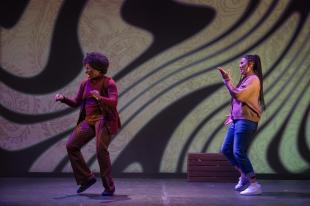 Two black women are dancing in front of a a swirly yellow and black backdrop.