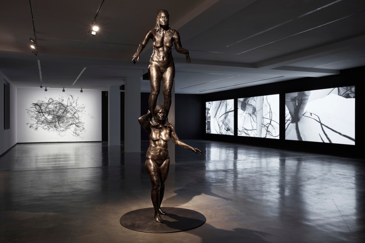 bronze statue of woman with another woman on shoulders in gallery setting. Julie Rrap.