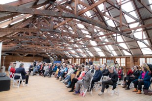 A huge repurposed wool shed with an audience inside looking to the left.