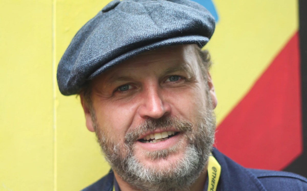 A Caucasian man with a greying beard and a grey flat cap is smiling at the camera.