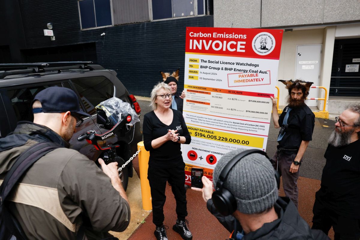 pvi Director Kelli McCluskey outside the BHP offices in Perth, standing in front of a giant poster that looks like an invoice from pvi to BHP.